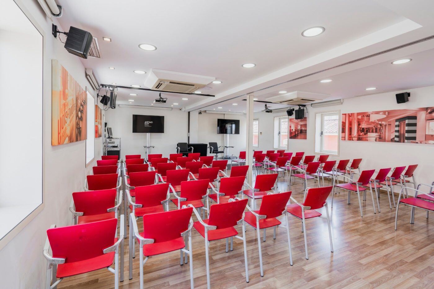 Sala de un encuentro anterior en Málaga, con filas de sillas rojas frente a una pantalla